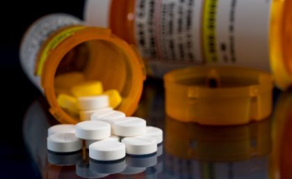 Image: Adobe a close up of a tipped over orange container with white pills spilling onto a black surface